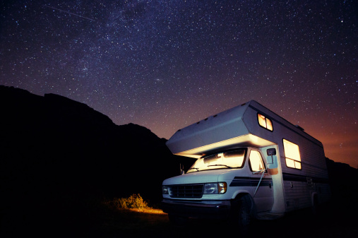 A small illuminated motorhome at night under the stars.